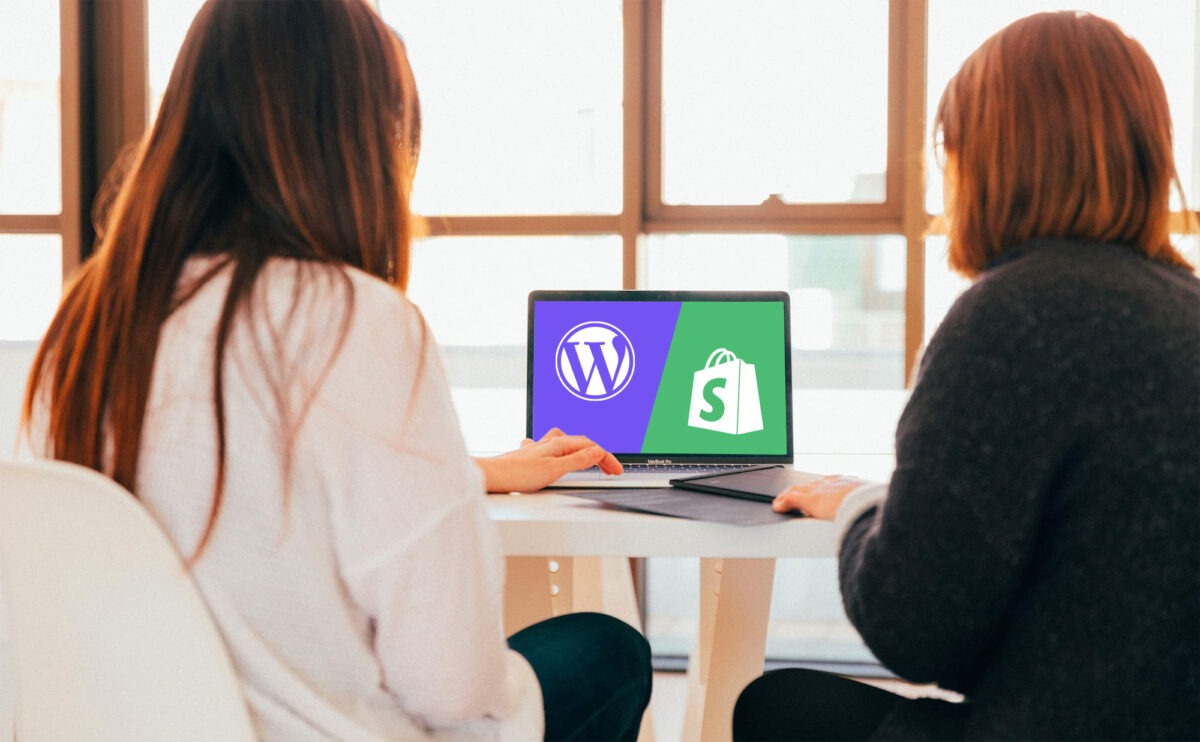 shot of two women with their backs turned, designing and browsing through a website in their office